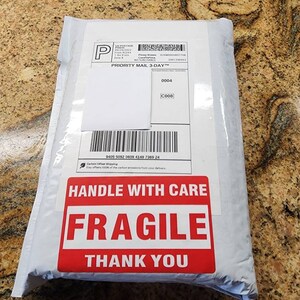 Peut inclure: Une enveloppe d'exp&eacute;dition rectangulaire blanche avec une &eacute;tiquette d'exp&eacute;dition Priority Mail 3-Day comprenant un code-barres et un num&eacute;ro de suivi. Un grand autocollant rectangulaire rouge porte le texte blanc HANDLE WITH CARE FRAGILE THANK YOU.