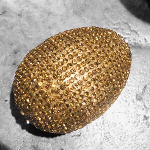 May include: A gold oval-shaped object covered in small, sparkling rhinestones.