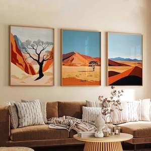 May include: Three abstract landscape paintings in gold frames hang on a wall above a brown sectional sofa with throw pillows. The paintings depict desert scenes with trees and red sand dunes.