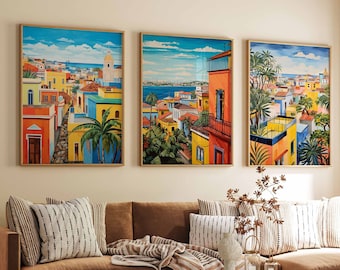 May include: Three framed art prints depicting colorful coastal town scenes. The artwork features vibrant buildings in shades of yellow, orange, and blue, with palm trees and a bright blue sky. The prints are displayed above a brown sectional sofa.