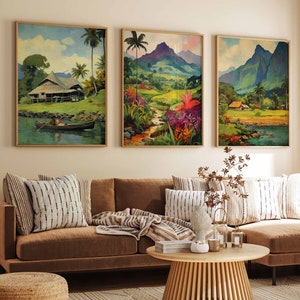 May include: Three framed landscape paintings showing tropical scenes with mountains, palm trees, and water. The paintings are in warm tones and hang above a brown sofa with striped cushions. A wooden coffee table and a woven rug complete the living room setting.