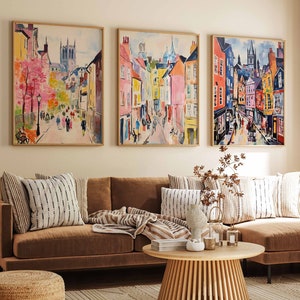 May include: A living room with a brown sectional sofa, three framed paintings of cityscapes, a wooden coffee table, a woven rug, and a woven footstool.