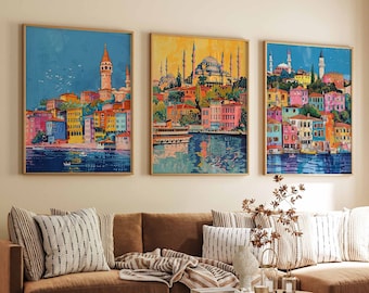 May include: Three framed landscape paintings depicting colorful cityscapes with water reflections. The artwork features buildings in various colors, including pink, blue, and yellow, with a warm, inviting aesthetic. The paintings are displayed above a brown sofa.
