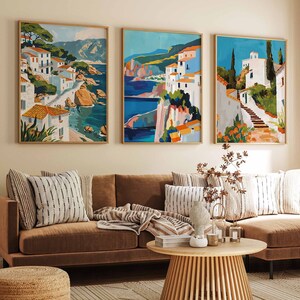 May include: A brown sectional sofa with white and brown striped cushions, a brown throw blanket, and a wooden coffee table. Three framed paintings of colourful landscapes with white buildings hang on the wall behind the sofa.