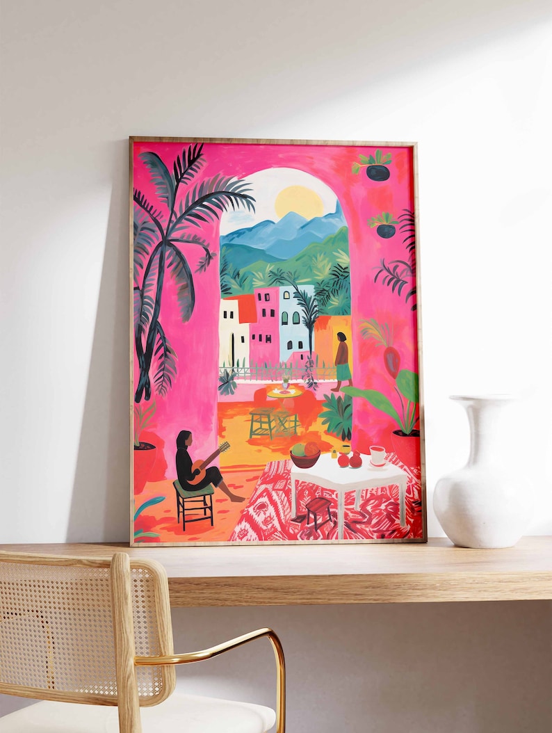 May include: A framed illustration of a pink and orange patio scene with a woman playing a guitar, a table with fruit, and a view of a town through an archway.