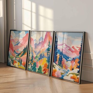May include: Three framed landscape art prints. Each print features a colorful watercolor painting of a mountain scene with trees and a river. The color palette includes pink, blue, yellow, and green. The frames are black.