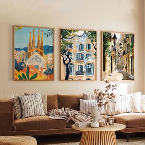May include: Three framed art prints depicting European cityscapes. The artwork features a cathedral, a building with balconies, and a narrow street with streetlights. The prints are displayed above a brown sofa with decorative pillows and a wooden coffee table.