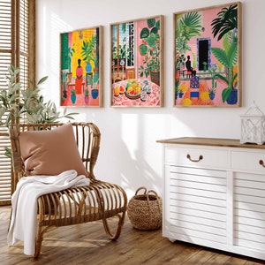 May include: Three framed illustrations of tropical scenes. The first shows a woman in a red dress standing in a lush green garden. The second shows a table with fruit and a vase of flowers in a room with a window. The third shows a person sitting on a bench in a garden with palm trees.