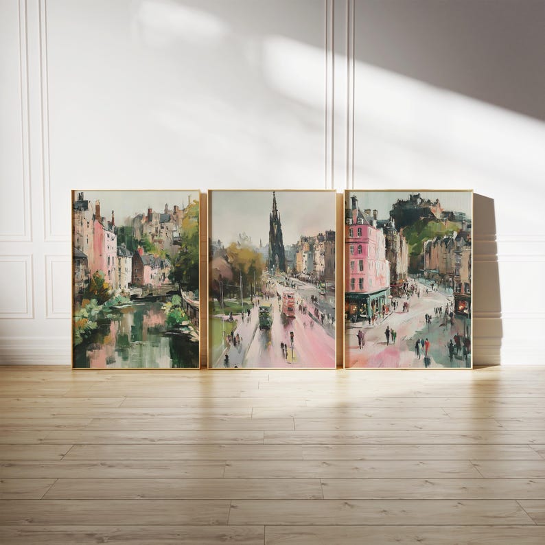 May include: Set of three framed watercolor prints depicting a city scene with buildings, a river, and a street with people. The artwork features a muted color palette with pink, green, and brown tones. The frames are gold.