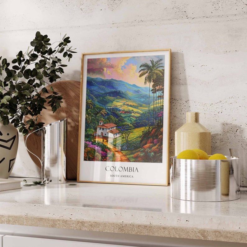 Op de afbeelding: Een ingelijste print van een kleurrijk landschap met palmbomen en een wit huis. De print is getiteld "COLOMBIA, SOUTH AMERICA".