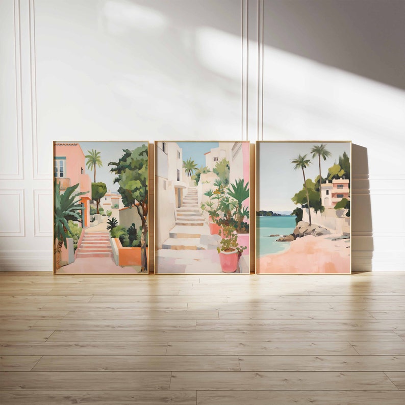 May include: Three framed paintings depicting a Mediterranean scene. The first painting shows a pink building with a staircase leading up to a street with palm trees and lush greenery. The second painting shows a similar scene with a staircase leading up to a street with palm trees and lush greenery. The third painting shows a beach scene with palm trees, a rocky shore, and turquoise water.