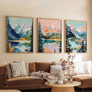 May include: Three framed landscape paintings of mountains and lakes. The paintings are in a modern style with bright colors and bold lines. The paintings are hung on a white wall above a brown couch.