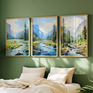 May include: Three framed landscape art prints. Each print features a river flowing through a valley with mountains and trees. The artwork has a watercolor style with blue, green, and brown tones. The frames are gold-colored.