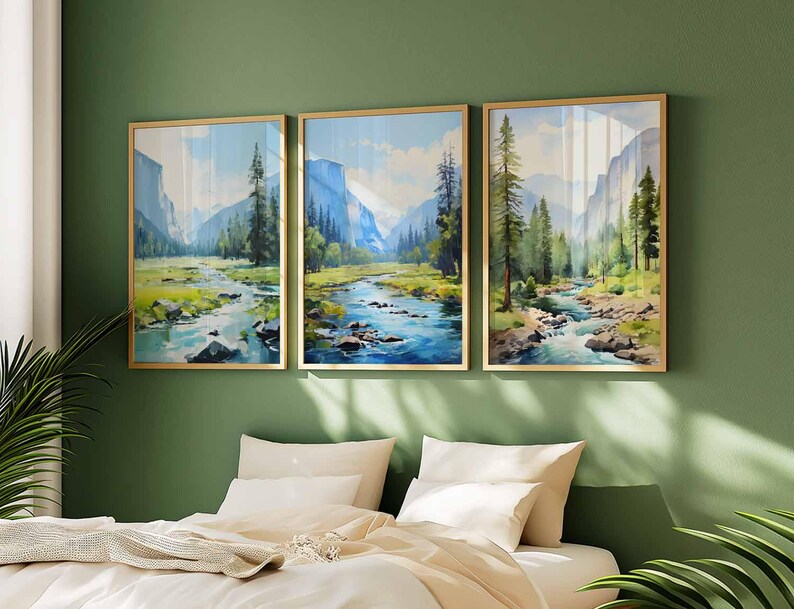 May include: Three framed landscape art prints. Each print features a river flowing through a valley with mountains and trees. The artwork has a watercolor style with blue, green, and brown tones. The frames are gold-colored.
