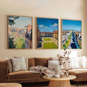 Könnte beinhalten: Drei gerahmte Bilder von Stadtansichten. Die Bilder befinden sich in einem Wohnzimmer mit einem braunen Sofa und einem Holz-Couchtisch. Die Bilder haben alle einen ähnlichen Stil, mit dem Fokus auf die Gebäude und Straßen. Das erste Bild zeigt eine Ansicht einer Stadt von oben, mit den Gebäuden im Vordergrund und dem Himmel im Hintergrund. Das zweite Bild zeigt eine Ansicht eines Stadtplatzes, mit den Gebäuden, die den Platz umgeben. Das dritte Bild zeigt eine Ansicht einer Stadtstraße, mit den Gebäuden, die die Straße säumen.