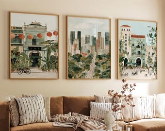 May include: Three framed watercolour prints of cityscapes. The artwork shows a building with red lanterns, a modern skyline, and a building with a tower. The prints are displayed above a brown sofa with striped cushions.