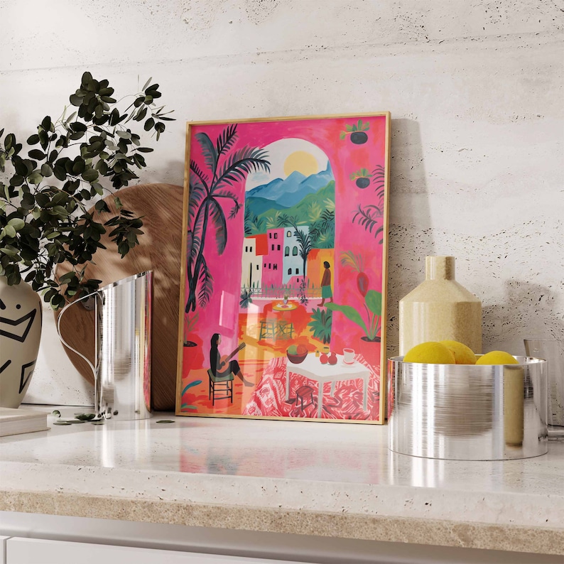 May include: A framed illustration of a pink building with a palm tree and a woman sitting on a chair. The illustration is set against a pink background with a blue sky and green hills in the distance.