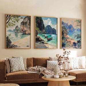 May include: Three framed paintings depicting tropical landscapes with lush green foliage, rocky cliffs, and turquoise waters. The paintings feature boats and a sandy beach.