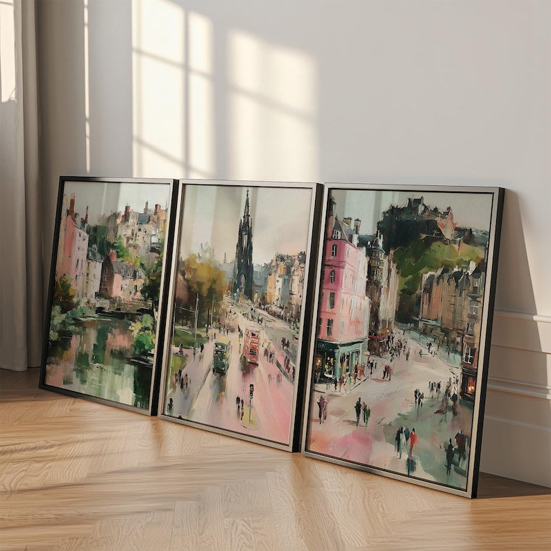 May include: Three framed watercolor prints of a city street scene. The artwork features buildings in shades of pink, brown, and green, with people and vehicles on the street. The frames are black with silver inner edges.