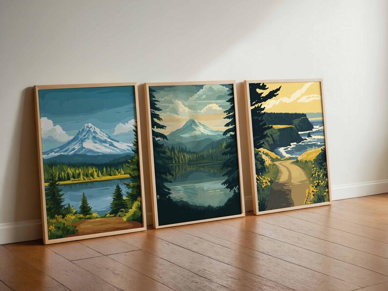 May include: Three framed landscape art prints. The prints depict mountain and lake scenes with a color palette of blues, greens, and yellows. The frames are made of light-colored wood. The art is leaning against a white wall on a wooden floor.