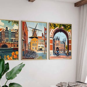 Pu&ograve; includere: Tre stampe artistiche incorniciate raffiguranti paesaggi urbani europei. L'opera presenta edifici colorati, mulini a vento e ingressi ad arco. Nelle scene sono visibili biciclette. Le cornici hanno una finitura dorata e l'arte &egrave; esposta su un muro bianco.