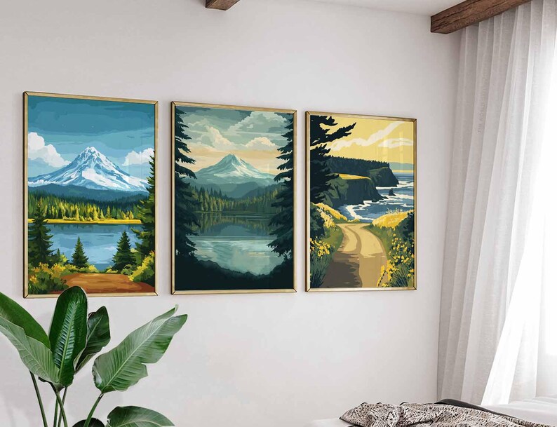 May include: Three framed landscape art prints. The prints depict mountain and lake scenes with a road leading to the coast. The color palette includes blues, greens, and yellows, with gold frames. The art is displayed on a white wall.