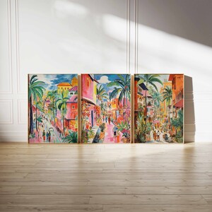 May include: A three-piece set of colorful paintings depicting a street scene in a tropical city. The paintings feature vibrant colors, palm trees, and buildings with pink and yellow accents. The paintings are framed in gold.
