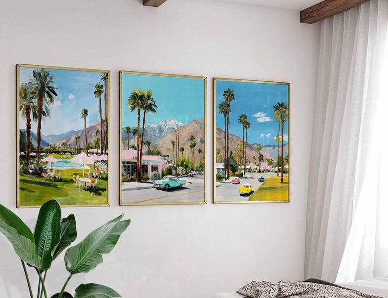 May include: Set of three framed landscape paintings. Each painting depicts a sunny scene with palm trees, mountains, and vintage cars. The paintings have gold frames and are displayed on a white wall.