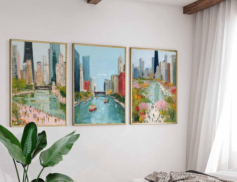 May include: Set of three framed cityscape paintings. Each artwork depicts a river scene with buildings, bridges, and people. The paintings feature a palette of blues, greens, pinks, and yellows, with gold frames. The artwork is displayed on a white wall.