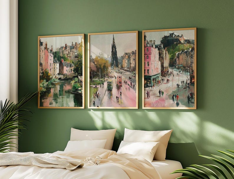 May include: Three framed landscape paintings with gold frames hang on a green wall above a bed. The paintings depict city scenes with buildings, streets, and people. The artwork has a watercolor style with pink, green, and brown tones.
