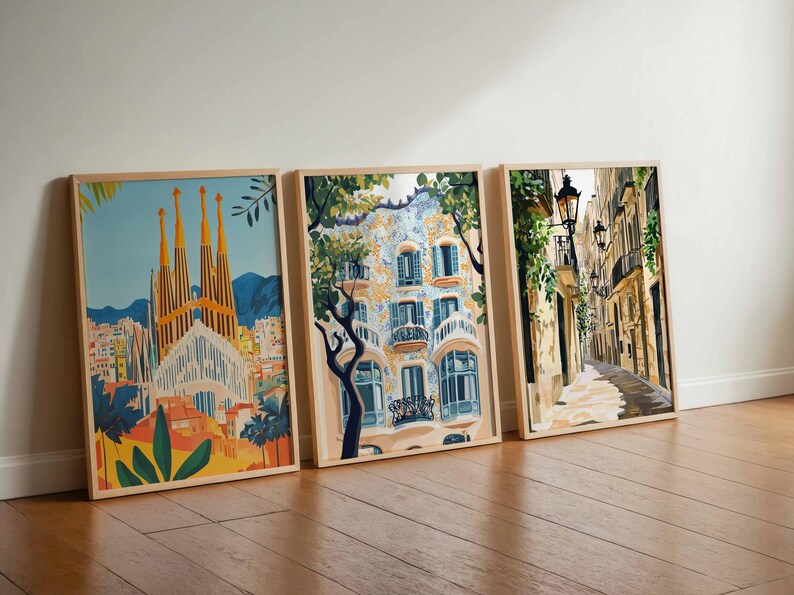 May include: Three framed art prints leaning against a wall. The prints depict architectural scenes, including a cathedral with tall spires, a building with ornate balconies, and a narrow street with streetlights. The frames are light-colored wood.