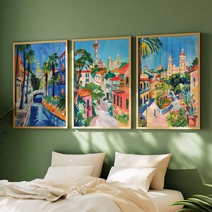 May include: Three framed paintings depicting colorful scenes of a European city with buildings, palm trees, and a canal. The paintings are in a modern style with bright colors and bold lines.