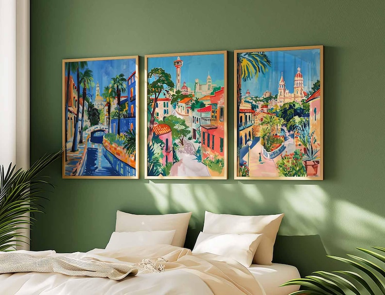 May include: Three framed paintings depicting colorful scenes of a European city with buildings, palm trees, and a canal. The paintings are in a modern style with bright colors and bold lines.