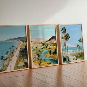 May include: Three framed landscape art prints. The artwork depicts coastal scenes with palm trees, beaches, and roads. The color palette includes blues, greens, and yellows, with a wooden frame.