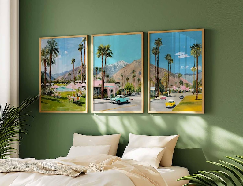May include: Three framed art prints depicting a retro Palm Springs scene with palm trees, vintage cars, and pink buildings. The artwork is set against a blue sky and mountain backdrop, framed in gold, and displayed on a green wall.