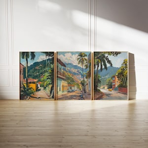 May include: A set of three framed paintings depicting a colorful street scene in a tropical location. The paintings feature vibrant colors, lush greenery, and buildings with terracotta roofs. The street is lined with palm trees and leads up a hillside.