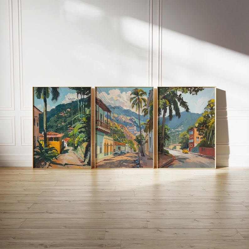 May include: A set of three framed paintings depicting a colorful street scene in a tropical location. The paintings feature vibrant colors, lush greenery, and buildings with terracotta roofs. The street is lined with palm trees and leads up a hillside.