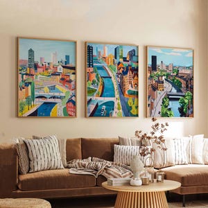 Könnte beinhalten: Drei gerahmte Bilder von Stadtansichten mit einem Fluss, der durch sie fließt. Die Bilder befinden sich in einem Wohnzimmer mit einer braunen Couch, einem Couchtisch und einer Pflanze.