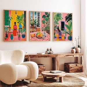 May include: Three framed illustrations of tropical scenes with vibrant colors and lush greenery. The first image features a woman in a pink dress standing in a room with plants. The second image shows a table with fruit and a vase of flowers. The third image depicts a person sitting in a room with plants and a doorway.