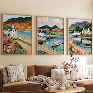 May include: A set of three framed landscape paintings depicting coastal scenes with white houses, sailboats on calm water, and mountains in the background. The artwork features vibrant colors including green, blue, orange, and pink, with floral foregrounds.