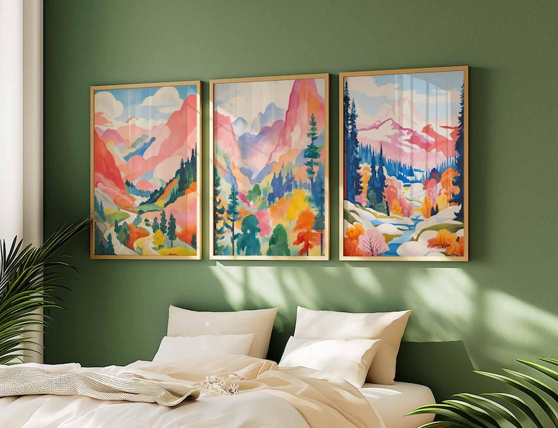 May include: Three framed landscape art prints. Each print features a colorful watercolor painting of a mountain scene with trees and a river. The artwork is in shades of pink, blue, green, yellow, and orange. The frames are gold.