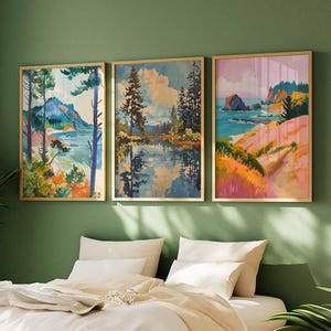 May include: Three framed landscape paintings with gold frames hang above a bed. The paintings depict colorful scenes of nature, including mountains, lakes, and coastal views. The artwork features a variety of colors, including blues, greens, pinks, and oranges.
