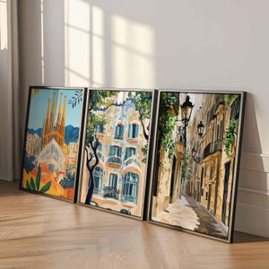 May include: Three framed art prints depicting architectural scenes. The first print showcases a cathedral with tall spires, the second a building with blue and white details, and the third a narrow street with street lamps. The frames are black.