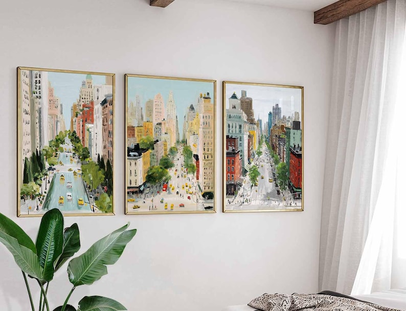 May include: Three framed cityscape paintings. Each features a street scene with tall buildings, trees, and yellow taxis. The artwork has a gold frame and is mounted on a white wall. The paintings are in a row, creating a cohesive display.