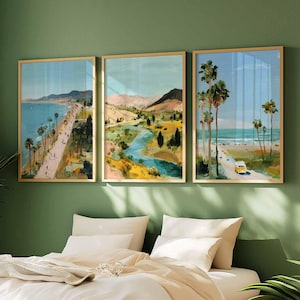 May include: Three framed landscape art prints. The artwork depicts coastal scenes with palm trees, roads, and mountains. The color palette includes blues, greens, and yellows. The frames are gold-colored, and the art is displayed above a bed with white linens.