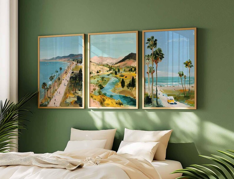 May include: Three framed landscape art prints. The artwork depicts coastal scenes with palm trees, roads, and mountains. The color palette includes blues, greens, and yellows. The frames are gold-colored, and the art is displayed above a bed with white linens.
