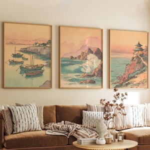 May include: Three framed art prints depicting coastal scenes in a traditional Japanese style. The artwork features boats, crashing waves, and a pagoda, all rendered in soft pastel colors with a vintage aesthetic. The frames are a light wood color.
