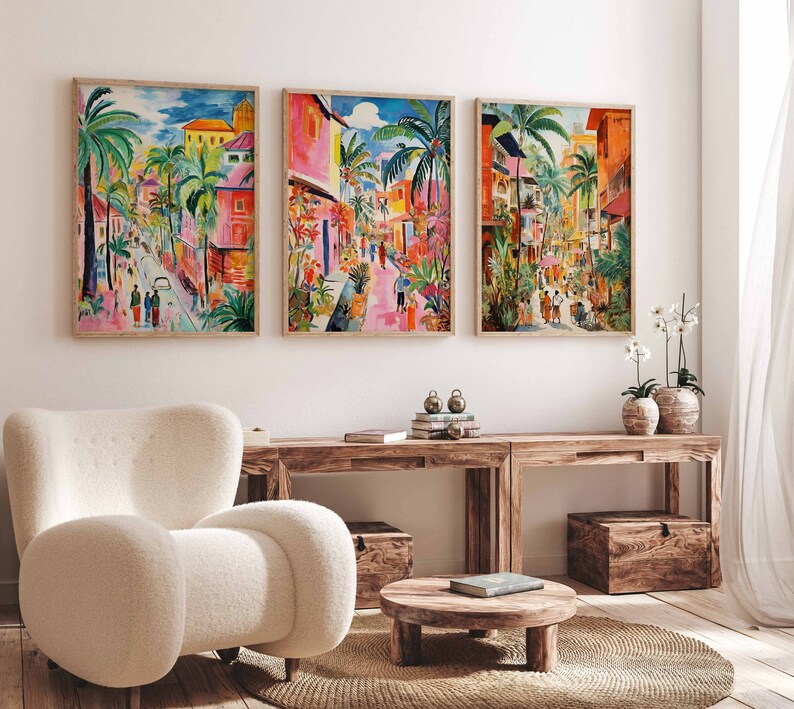 May include: Three colorful paintings of a street scene with palm trees, buildings, and people walking. The paintings are framed in wood and hung on a white wall.