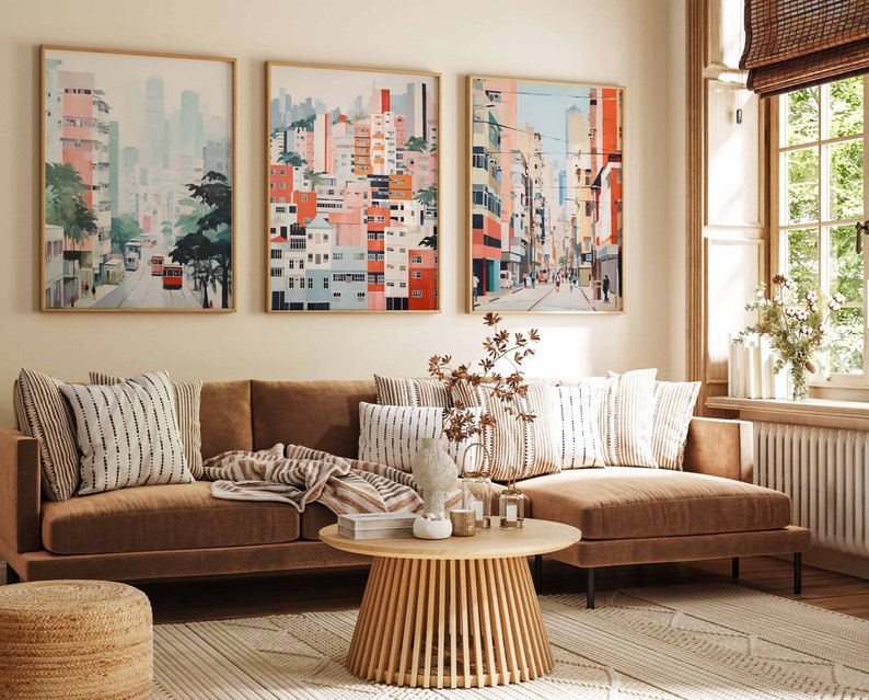 May include: A brown sectional sofa with a light brown throw blanket and a light brown and white striped throw pillow. The sofa is in front of a wall with three framed pictures of cityscapes. The pictures are in a light wood frame and have a white mat. The sofa is in a living room with a wooden coffee table and a light brown rug.
