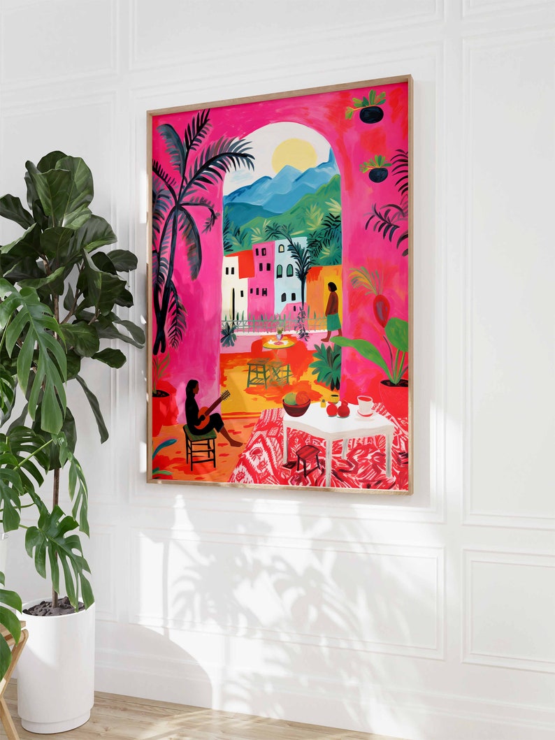 May include: A colorful painting of a pink building with a view of a mountain range and a palm tree. The painting is framed in a wooden frame.